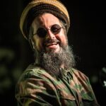 Nonpalidece en Rosario — cantante con gorro rasta y lentes redondos sonriendo durante un show