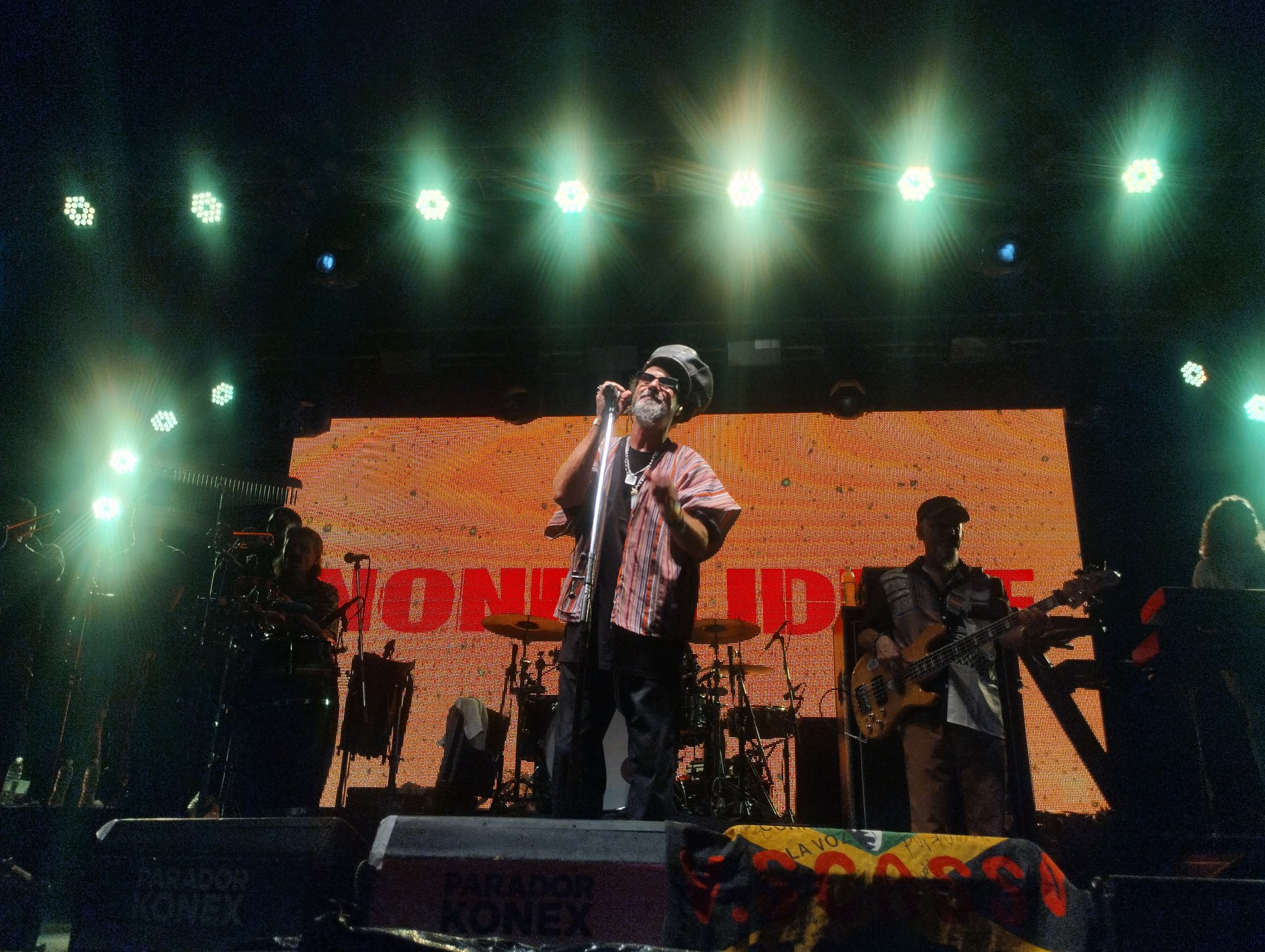 Nonpalidece en vivo — el cantante frente al micrófono con la banda y el logo de fondo en pantalla
