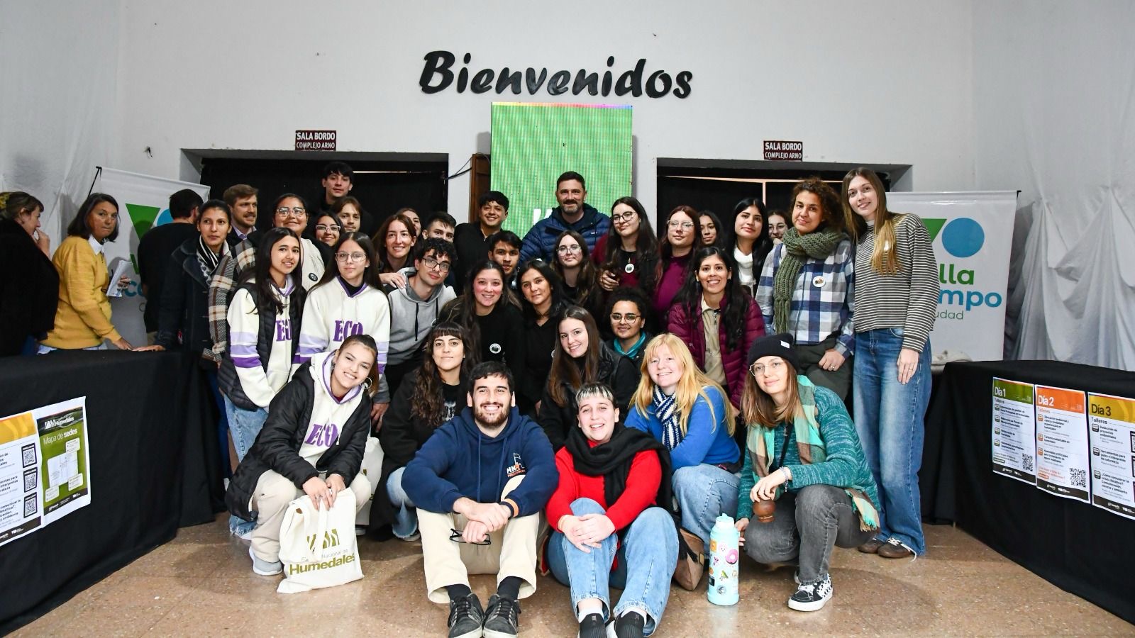 Participantes y jóvenes del Foro Nacional de Humedales en Villa Ocampo junto al cartel de bienvenida