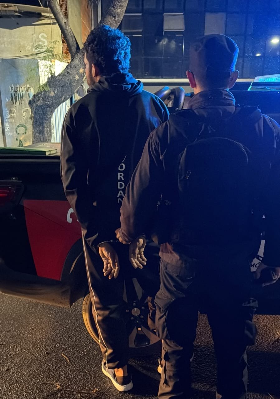 Un efectivo de la Brigada de Orden Urbano traslada de espaldas al hombre aprehendido, junto a un móvil policial