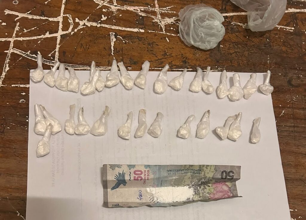 Decenas de envoltorios de nylon con material blanquecino ordenados sobre una hoja, junto a un billete doblado