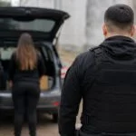 Operativo por una estafa en Funes: dos personas junto al baúl de un vehículo con mercadería y un policía de espaldas