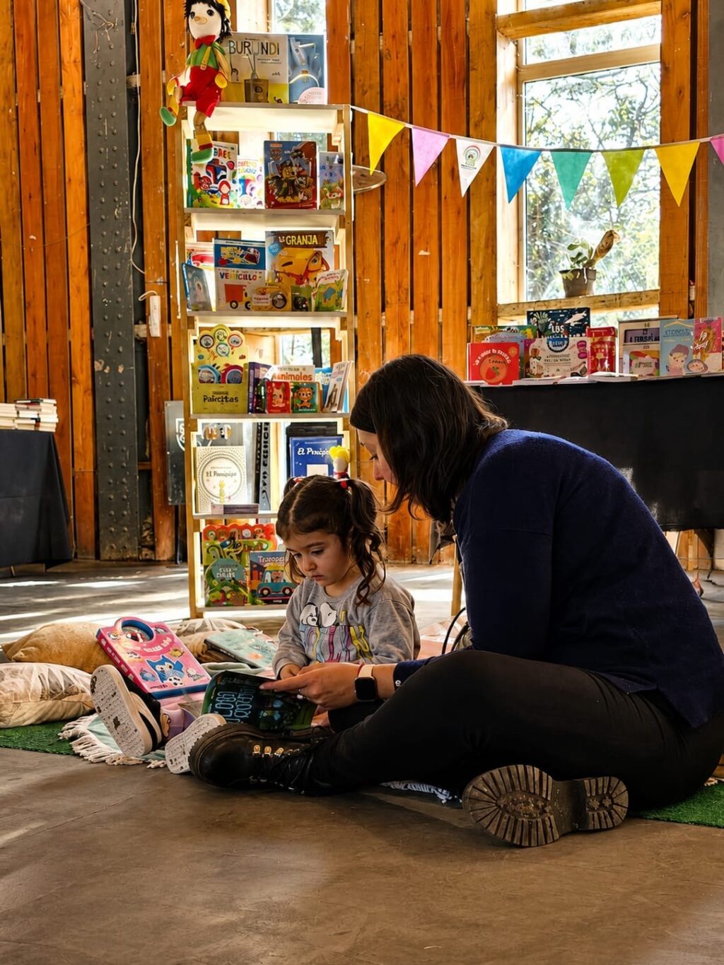 Una mujer y una niña leen un libro sentadas en el piso, junto al sector infantil de la Feria del Libro Funes 2026