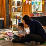 Arranca la primera Feria del Libro Funes 2026: una jornada de espectáculos para toda la familia Una mujer y una niña leen un libro sentadas en el piso, junto al sector infantil de la Feria del Libro Funes 2026