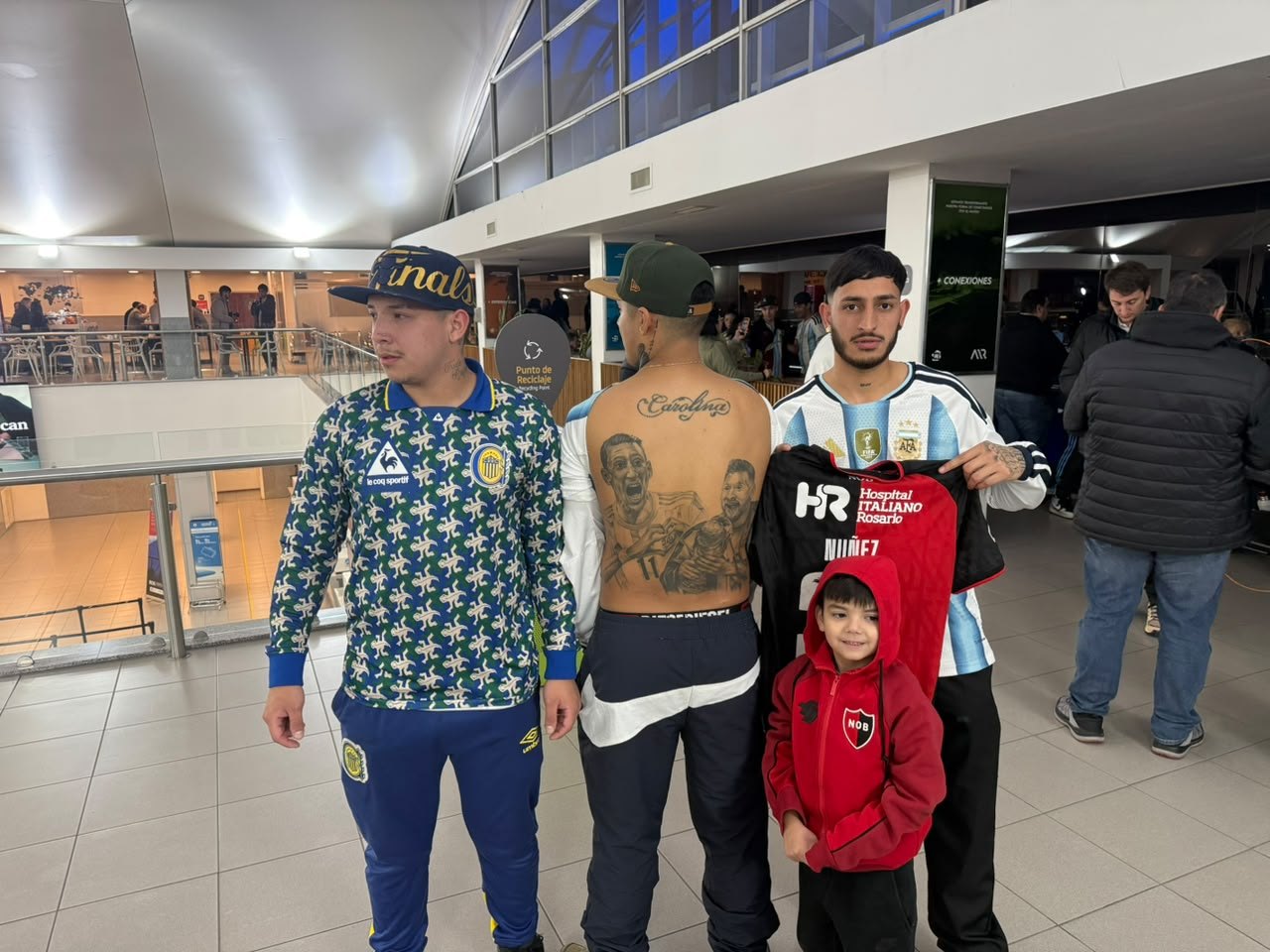 Un grupo de hinchas con camisetas de Rosario Central, Newell’s y la Selección argentina en el hall del aeropuerto