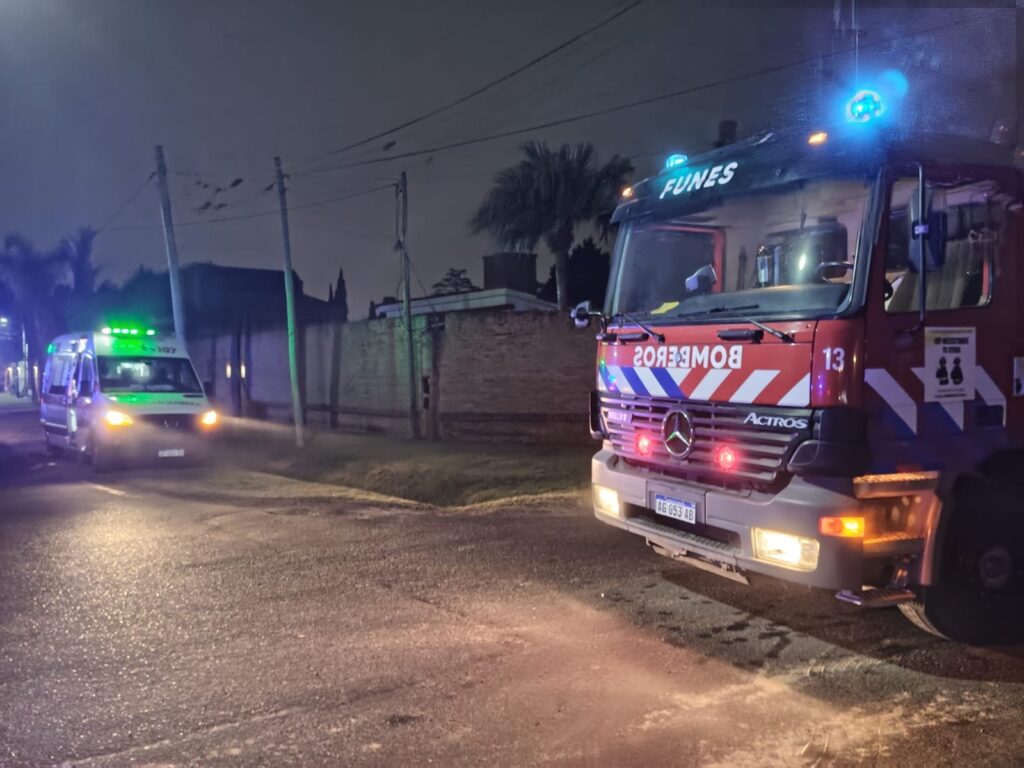 Una autobomba de Bomberos Voluntarios de Funes y una ambulancia del Sies frente a la vivienda incendiada, de noche