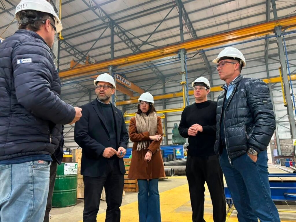Funcionarios y personal con cascos recorren el taller metalúrgico de RAFA S.A., con estructuras y puentes grúa al fondo