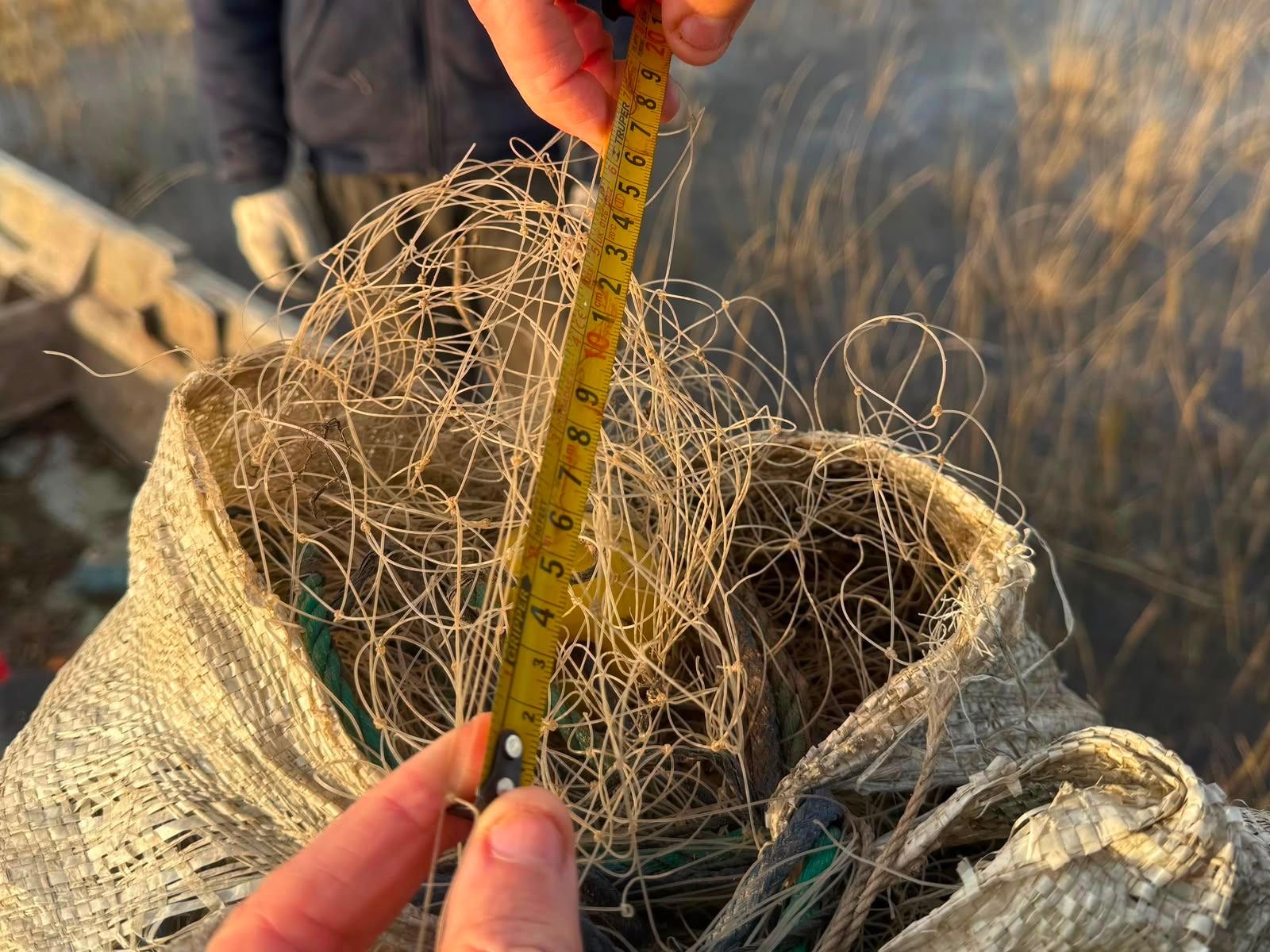Un inspector mide con cinta métrica la malla de una red de pesca secuestrada por estar fuera de reglamento
