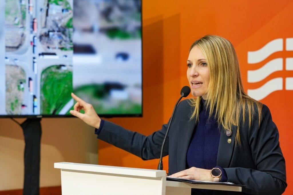 Virginia Coudannes habla en un atril frente a una pantalla con imágenes satelitales de una ruta